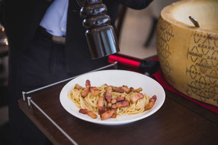 Spaghetti Carbonara made in cheese wheel topping with fried bacon on white plate.のeditorial素材