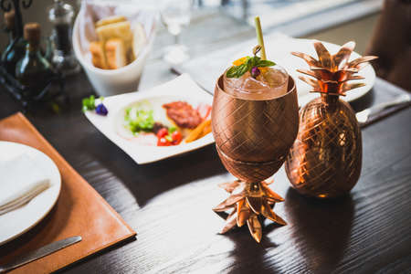 Cocktail served inside copper pineapple cup with dishes in the background.の写真素材