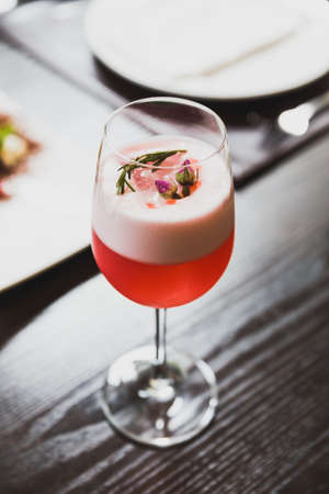 Red cocktail in wine glass topping with foam, flowers and rosemary.の写真素材