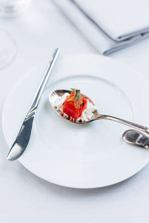 Modern French food: Diced watermelon with white crush cheese served in silver spoon on white plate with cutlery as appetizer.の写真素材