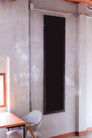 Long vertical black board on concrete wall at the cafe with grey chair.