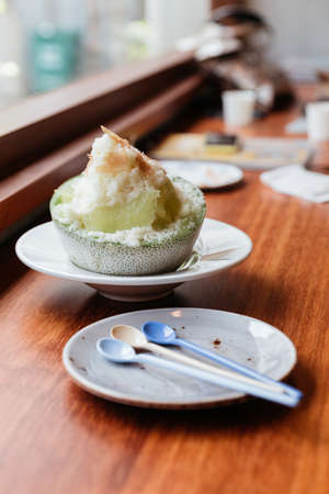 Japanese melon KakigÅri (shaved ice dessert) served in half of melon and sliced Pama Ham. With Dessert spoons in plate.の写真素材