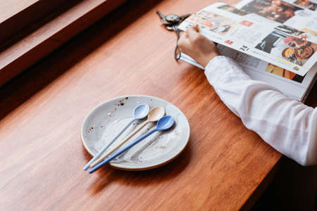 Dessert spoons in plate on wooden table with hands fliping magazine.の写真素材