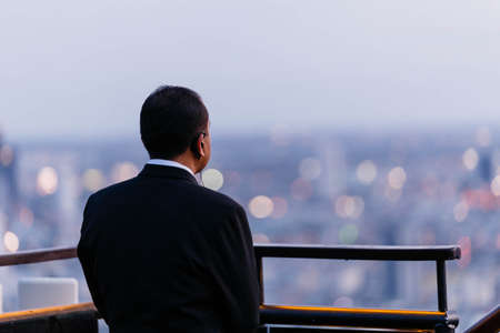 Close up Back of the Waiter in black suit is seeing cityscape at the dusk in Bangkok, Thailand.の写真素材