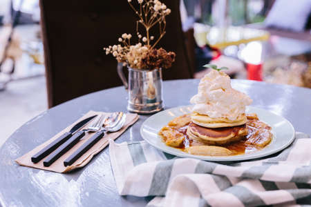 Pancakes with caramel-banana syrup topping with whip cream and mint leaves. With spoon, fork and knife, in blue plate over fabric with blue stripes.の写真素材