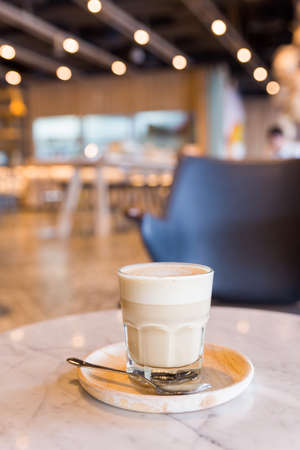 Hot latte in a glass cup with spoon and wooden plate.の写真素材