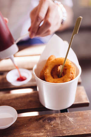 Onion rings served in white paper cup on wooden top table with sunlight.