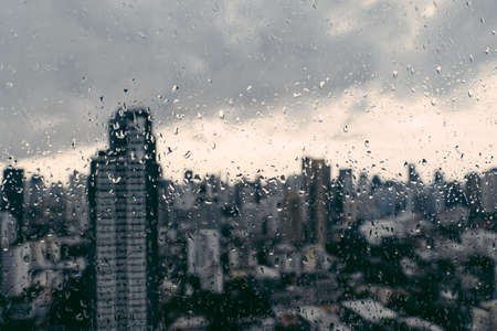 Rain over Bangkok: Out of focus cityscape behind the window glass with rain drops.の写真素材