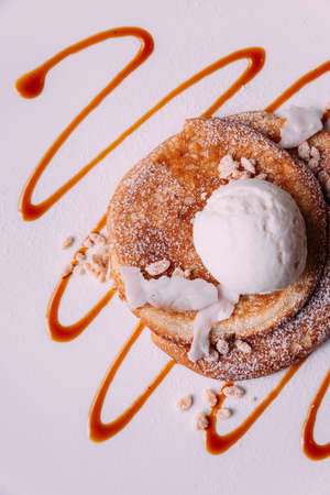 Top view of Pancakes topping with a scoop of coconut ice cream, coconut meat, crispy rice and icing over caramel lines on white plate.の写真素材