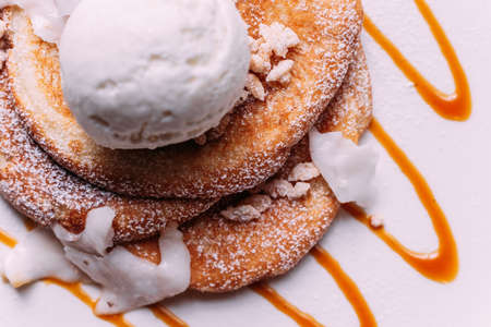 Close up Pancakes topping with a scoop of coconut ice cream, coconut meat, crispy rice and icing over caramel lines on white plate.の写真素材