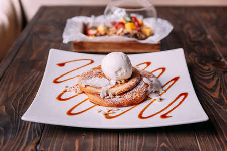 Pancakes topping with a scoop of coconut ice cream, coconut meat, crispy rice and icing over caramel lines on white plate.の写真素材