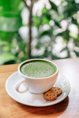Hot and smooth green tea latte with froth served in white ceramic cup with biscuitsの写真素材