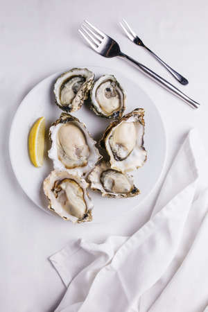 Top view of Fresh oysters served in white plate with sliced of lemon on white tablecloth.