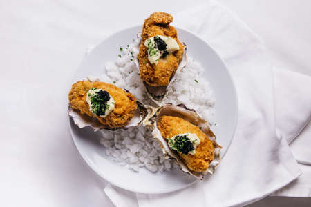 Top view of Deep fried oysters topping with mayonnaise and caviar served in white plate with sea salt decorated.の写真素材