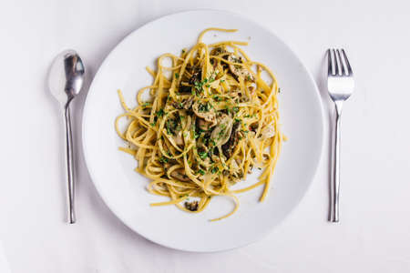 Top view of Oyster spaghetti served in white plate on white tablecloth.