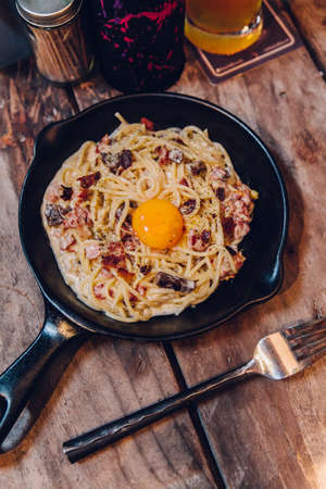 Fettuccine Carbonara yolk bacon served in black pan on wooden table.の写真素材