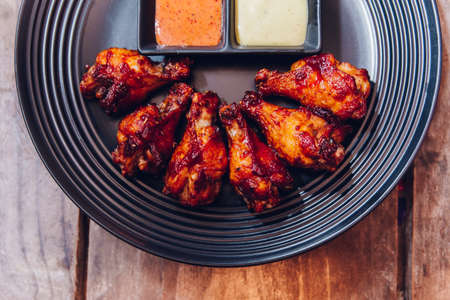 Buffalo chicken wings served with mayonnaise and thousand island sauce in black plate.