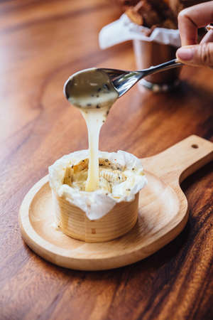 Sticky Brie cheese on wooden board served with green oak salad and fresh baked sliced bread.の写真素材