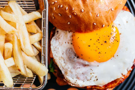 Close up Tasty burger with fried egg served with fries in black plate on wooden table.の写真素材