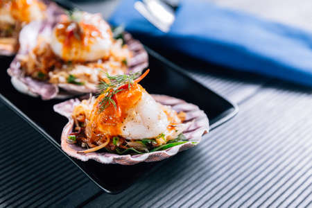 Grilled scallop in shell with spicy pomelo salad served in black plate.