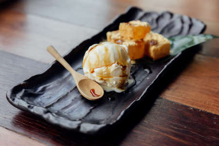 Warabi Mochi served with a scoop of vanilla ice cream that topping with caramel served in black plate.の写真素材