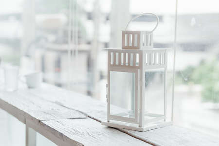 White old lamp on white painted wooden table with glass window and trees in background.の写真素材