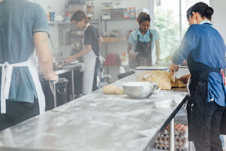 Artisans making bread on top aluminium table with flour over table.