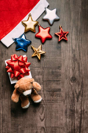 Santa hat with metallic stars, present and teddy bear on wooden background. Flat lay for Christmas and happy new year banner.の写真素材