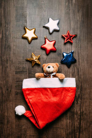 Santa hat with teddy bear inside and metallic stars on wooden background. Flat lay for Christmas and happy new year banner.の写真素材