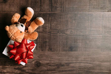 Present with red ribbon and teddy bear on wooden background. Flat lay for Christmas and happy new year banner.の写真素材