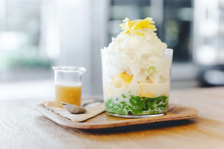 Lod Chong, Thai melon, puffed rice with coconut snow ice topping with sliced jackfruit. Served with caramel on wooden table with blur background.の写真素材