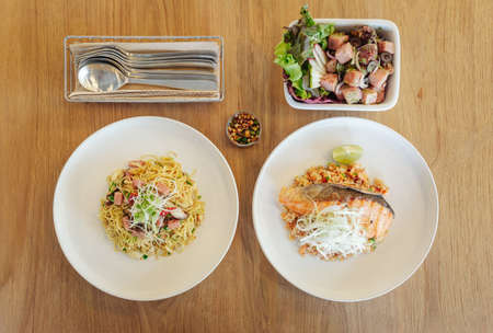 Stir fried Chinese noodle with ham and crab meat, Garlic fried rice with grilled salmon and Thick cut smoked ham spicy salad with black olives on wooden table.の写真素材