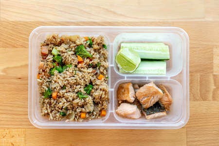 Top view of Organic fried salmon diced steak with onion, broccoli and carrot fried rice served with cucumber and lime in food grade box.の写真素材