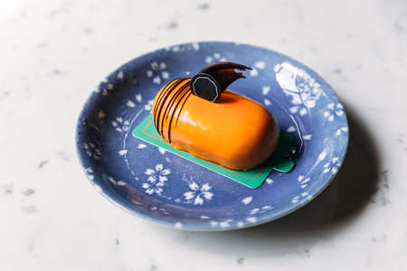 Classic Thai Tea Mousses Cake decorated with chocolate in blue plate on marble top table.
