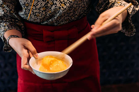 Woman wearing kimono is beating hen egg with chopsticks for dipping with sukiyaki beef.の写真素材