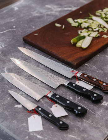 Many kinds of super sharp Japanese kitchen knives with ultra thin slice zucchini on wooden chopping board.の写真素材