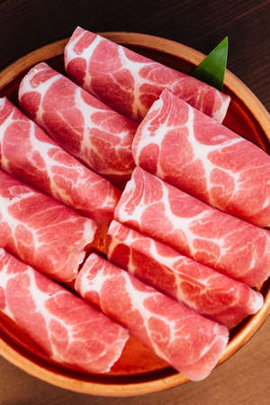 Close up Premium Rare Slices Kurobuta (Black Pig) pork with low-marbled texture on circle wooden plate served for Sukiyaki and Shabu.の写真素材