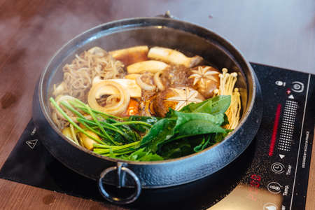 Sukiyaki hot pot with boiling vegetables including cabbage, konjac noodle, onion, carrot, shiitake, enokitake and tofu in Shoyu sauce soup.の写真素材