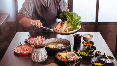 A woman pinching vegetables into hot pot by tongs with Wagyu A5 beef and sliced Kurobuta in Shabu clear soup with stream.の写真素材