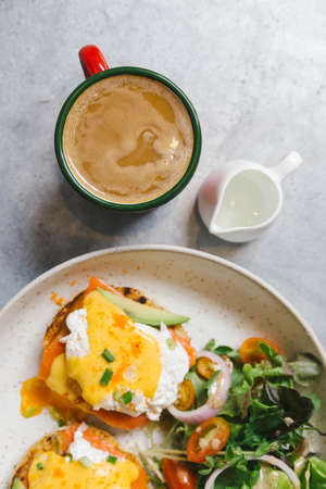 Top view of Egg Benedict with salmon and avocado, Served with salad in white plate. Served with hot...