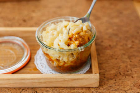 Female hand is scooping Macaroni Cheese Baked with meat sauce in glass bowl.