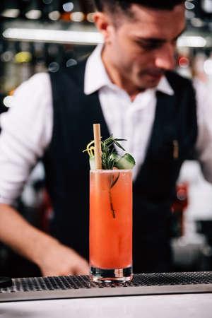 Male mixologist is making red cocktail and neatly decorating with sliced cucumber over cocktail...