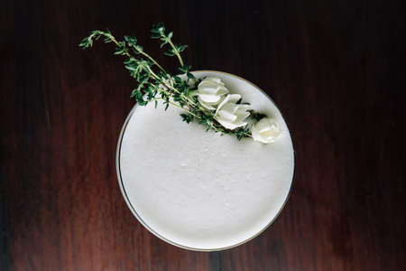 Top view of Yellow Cocktail with white foam decorated with white flower and green branch. Studio Shot.の写真素材