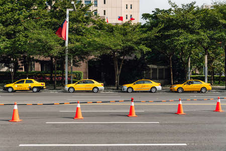 Four yellow taxis waiting for customers along the street that near the park with orange traffic cones, trees and building in the background in Taipei, Taiwanのeditorial素材