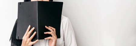 Muslim woman wearing hijab, white shirt and holding a black cover book in front of her with copy space.の写真素材