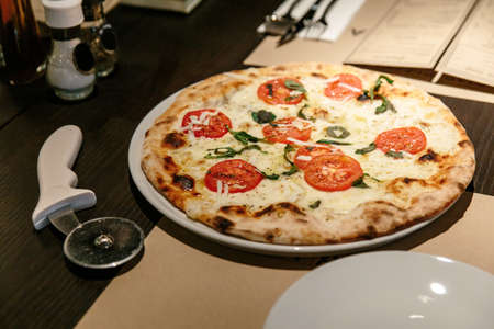 Hot Caprese Bianca Pizza from oven. Ingredients are Mozzarella, Parmesan, Olive oil, sliced tomato and Dough. Served on the table with Pizza Cutter.の写真素材