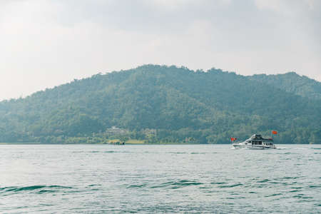 Travel boats floating over Sun Moon Lake with mountain in background in Yuchi Township, Nantou County, Taiwan.のeditorial素材