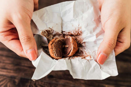 Cracked Chocolate Truffle made with a chocolate ganache center coated in chocolate, cocoa powder or chopped toasted nuts inside paper wrap that holding with hands.の写真素材