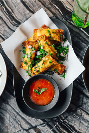 Top view of Fried Cheese Wontons sprinkle with scallion and shallot that served with chilli sauce.の写真素材