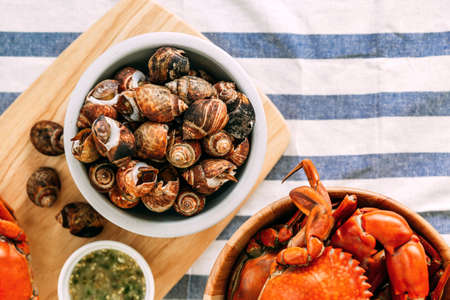 Top view of Grilled Laevistrombus Canarium in shells with Steamed Giant Mud Crabs in wooden bowl served with Thai spicy seafood sauce on white and blue stripes fabric.の写真素材